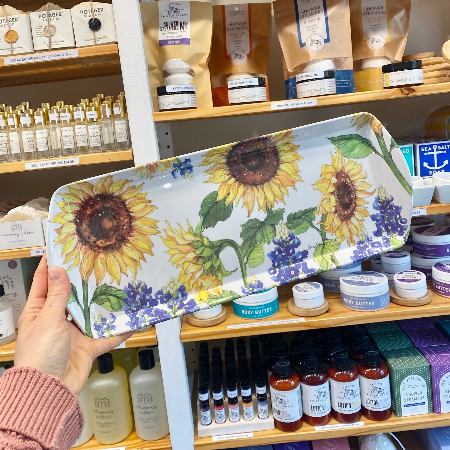 Person holding a decorative tray with sunflower design in front of a store shelf.