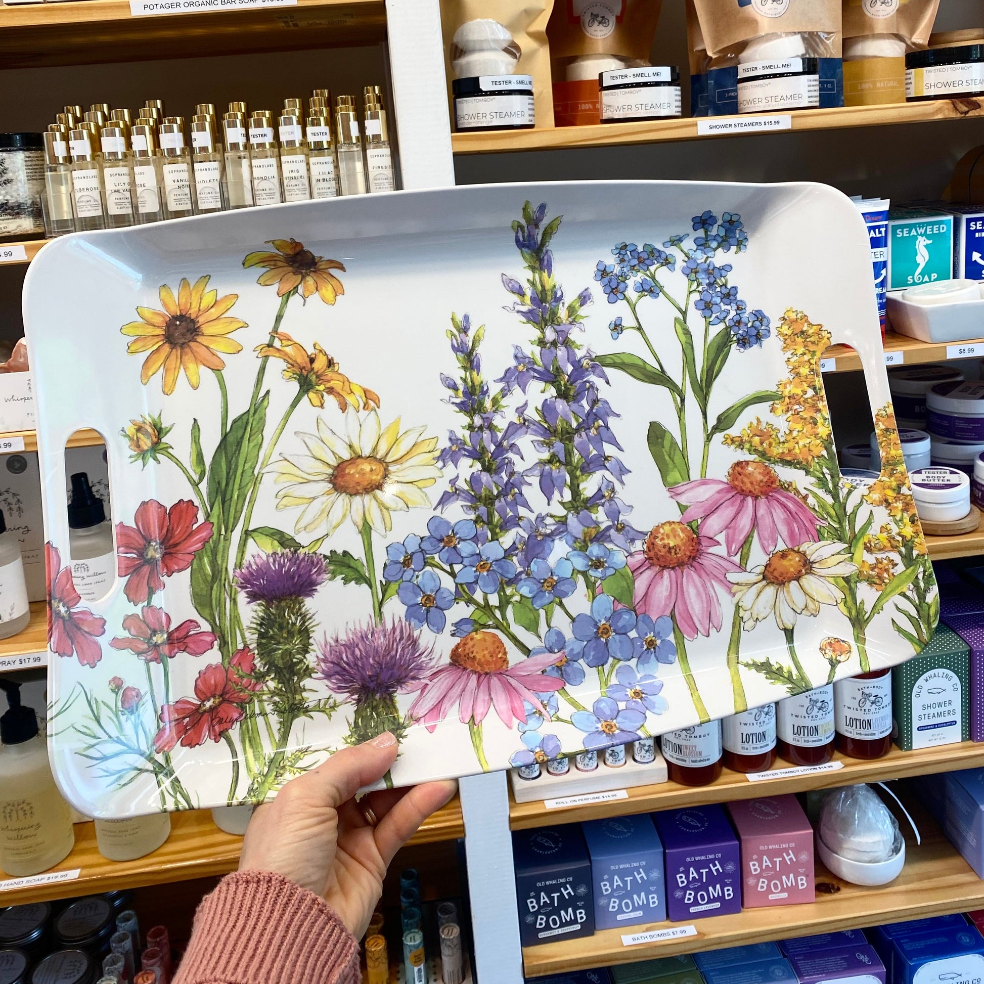 Hand holding a tray with floral design in front of a store shelf.