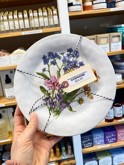 Decorative plate with floral design held in front of a store shelf.