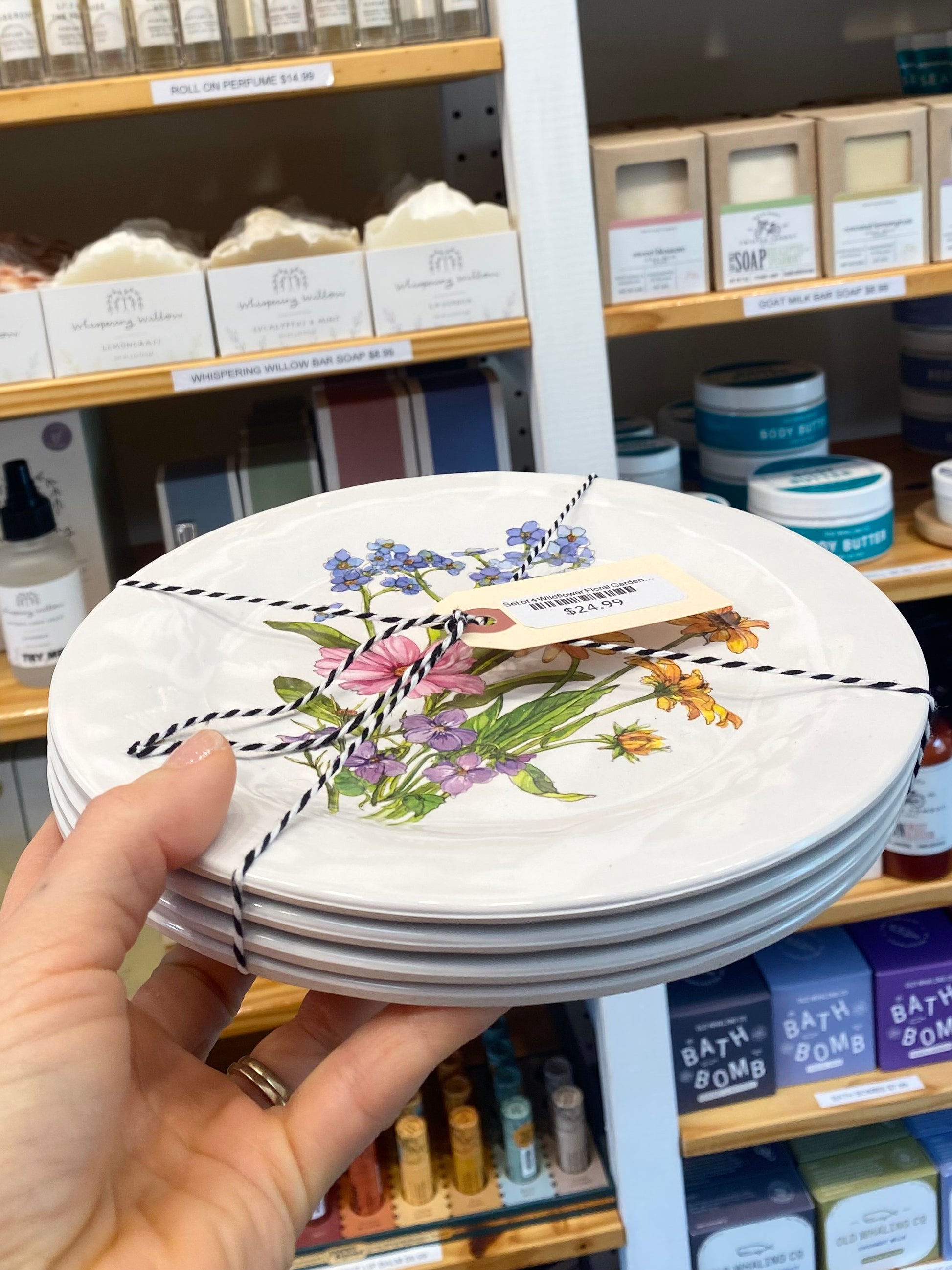Stack of decorative plates with floral design held in front of a store shelf with various products.