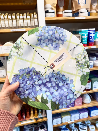Decorative plate with floral design held in front of a store shelf.