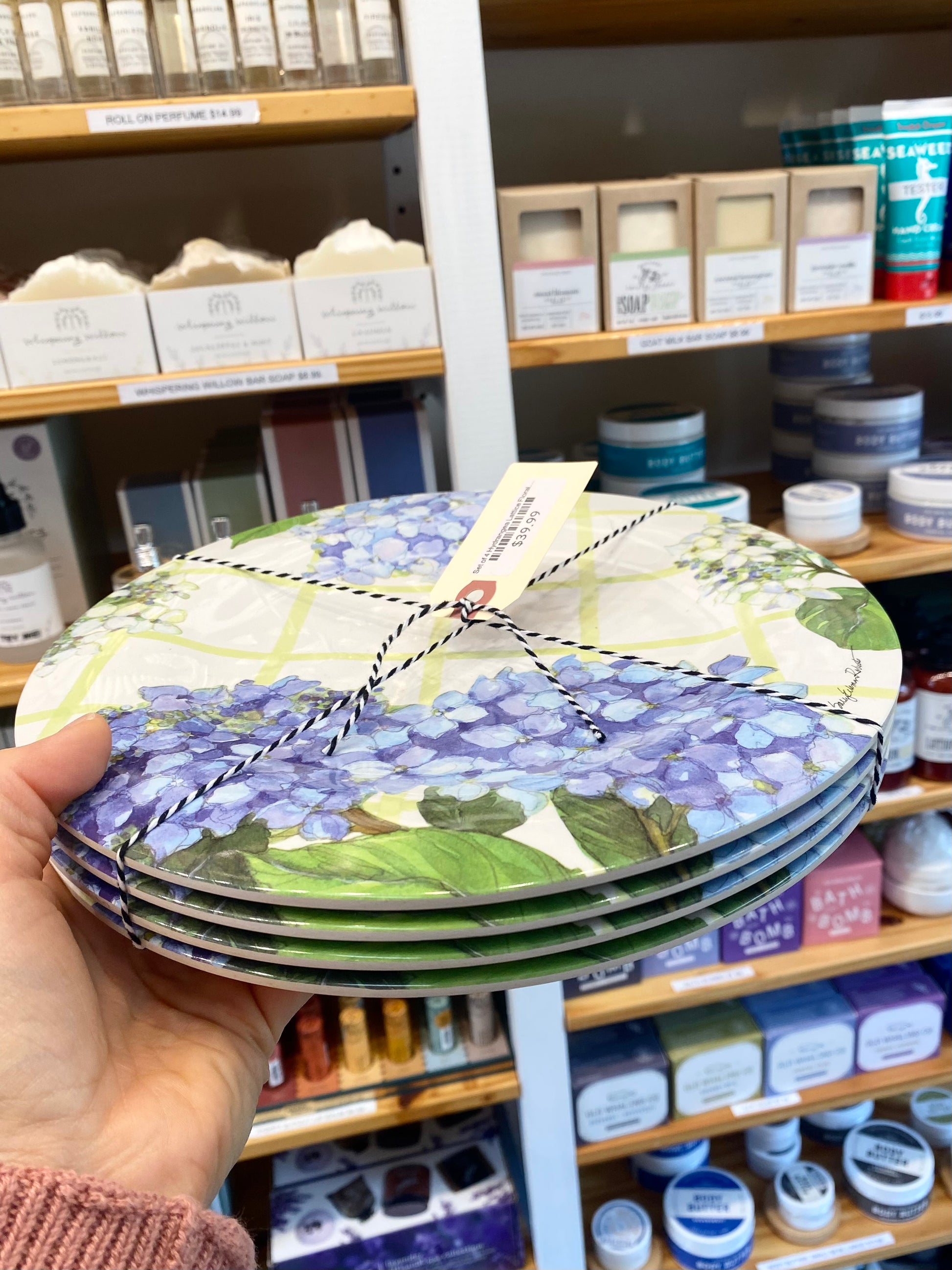 Stack of decorative plates with floral design held in front of a store shelf.
