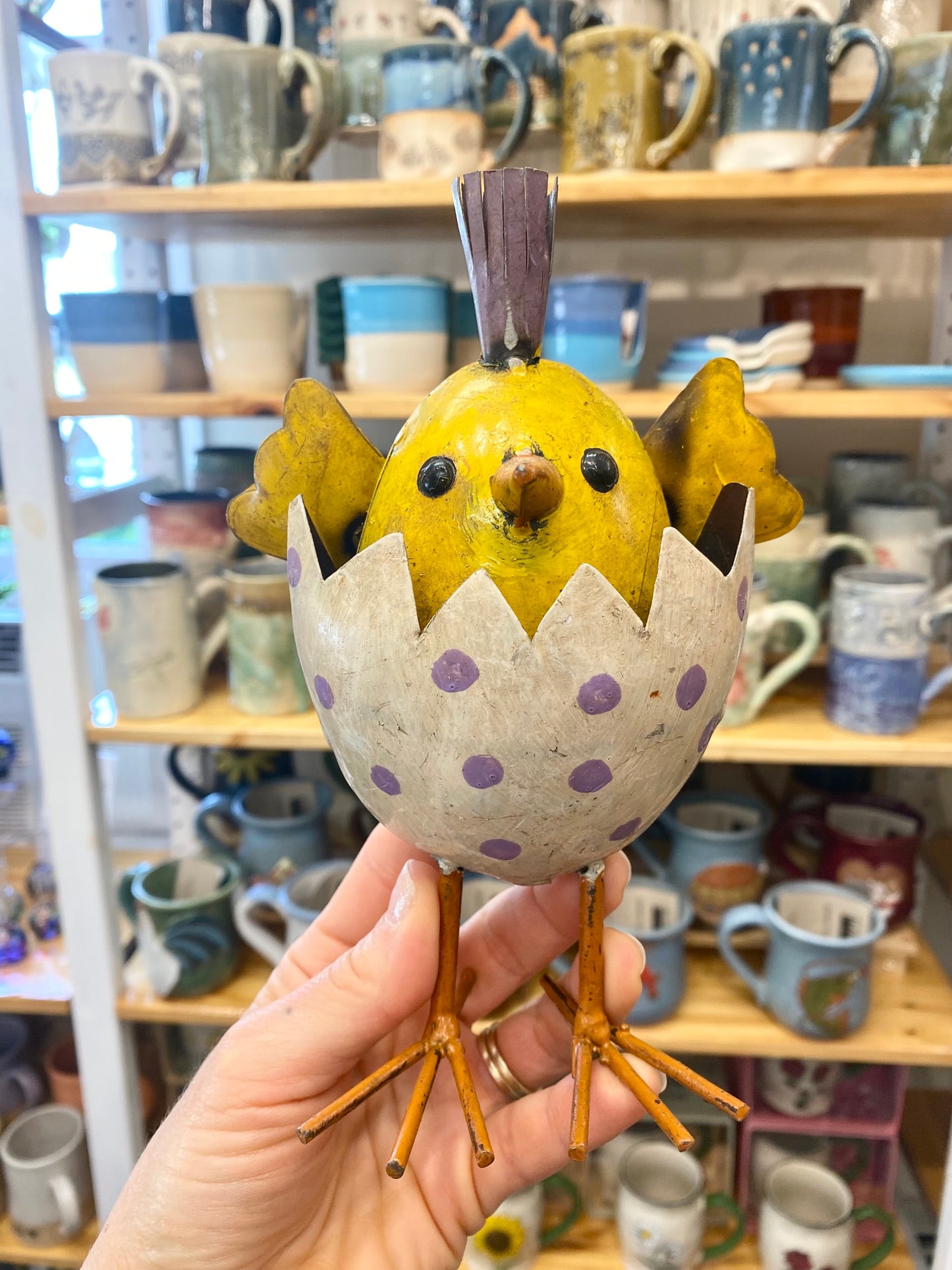 Decorative ceramic chick figurine held in front of a shelf with various ceramic items.