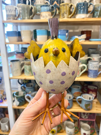 Decorative ceramic chick figurine held in front of a shelf with various ceramic items.