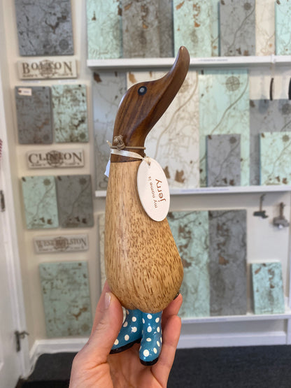 Wooden duck held by a hand, against a decorative tile background.