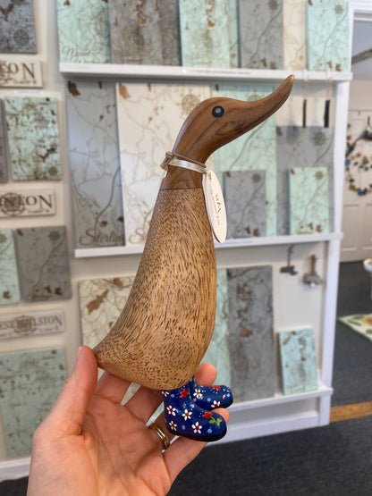 Wooden duck figure held by a hand in front of a map-themed wall.