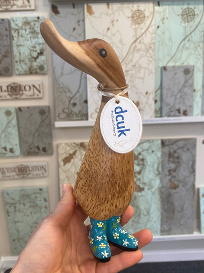 Hand holding a wooden duck figurine with a 'dcuk' label in front of a decorative wall.