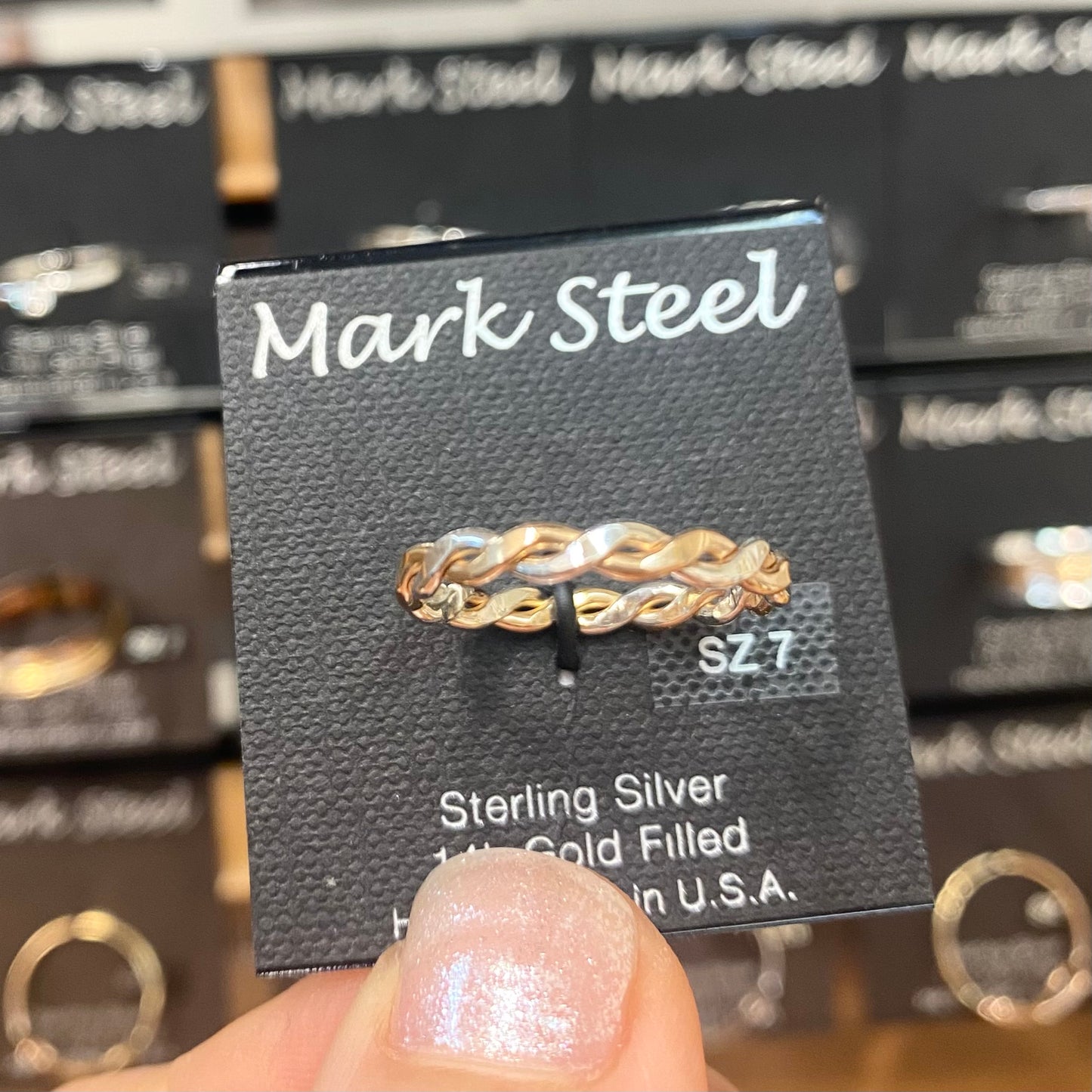 Gold and silver braided ring on a Mark Steel jewelry card held in front of a jewelry display. 