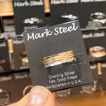 Gold and silver ring on a Mark Steel jewelry card held in front of a jewelry display. 