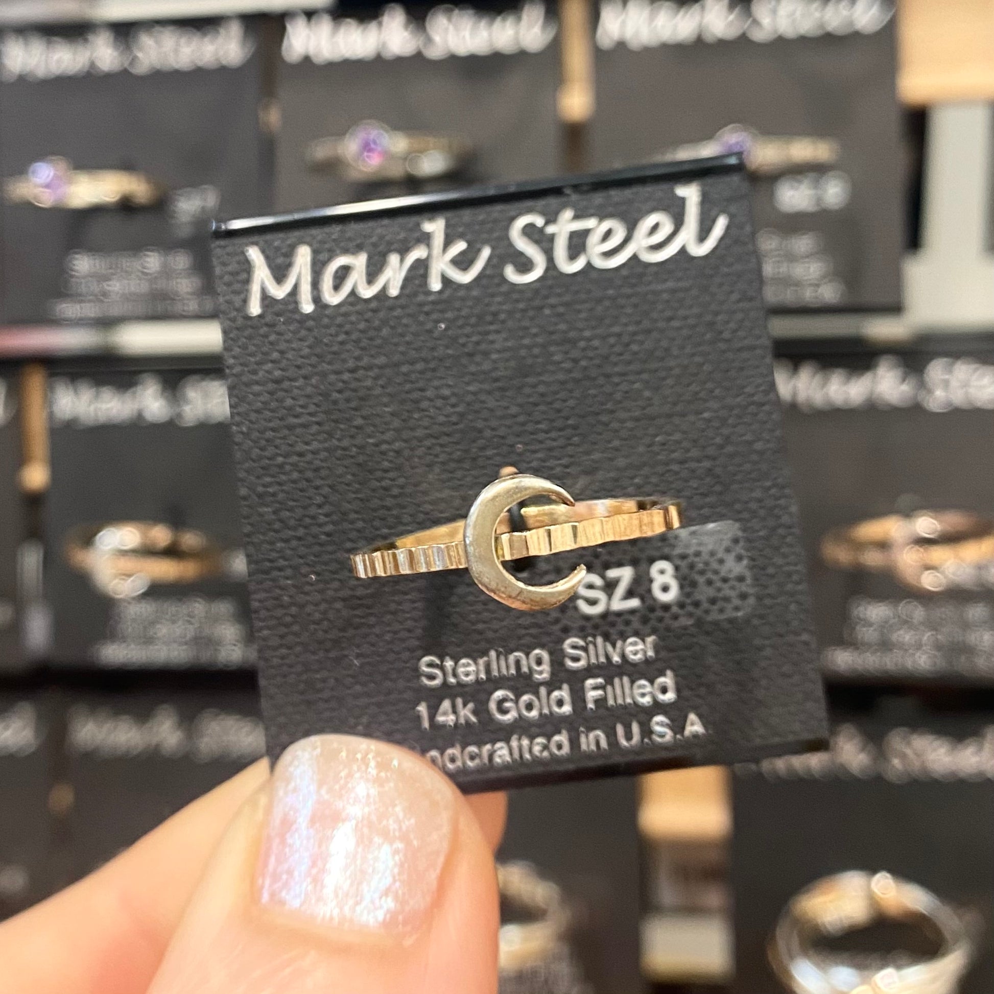 Gold and silver ring on a Mark Steel branded card with a blurred background of more rings.