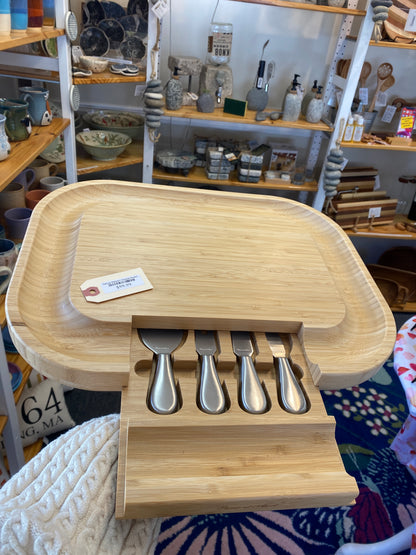 Wooden charcuterie board with partially open hidden drawer for cheese knives in a store setting