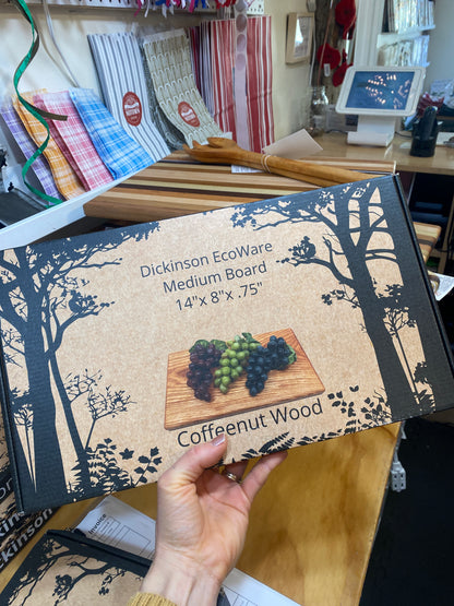 Hand holding a boxed cutting board with a wooden board design and text on a cluttered desk.