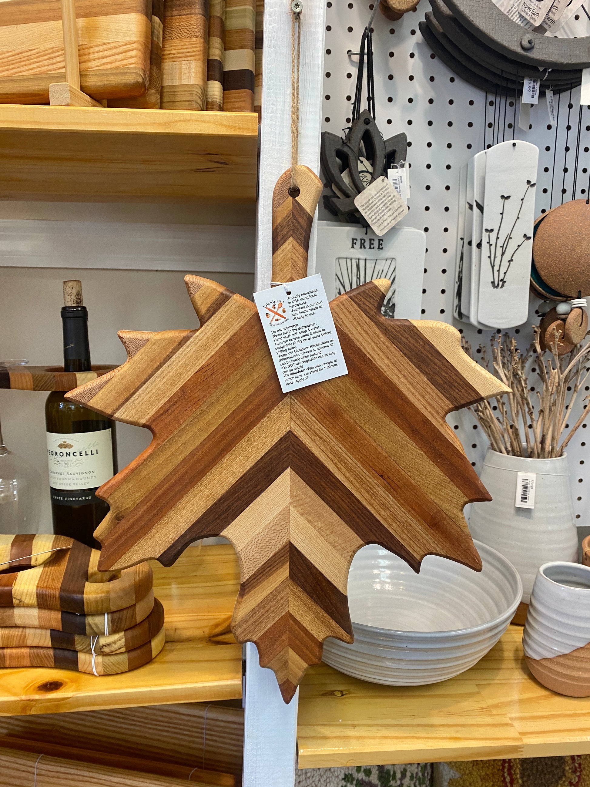 Wooden cutting board shaped like a leaf on a store shelf with other kitchen items.