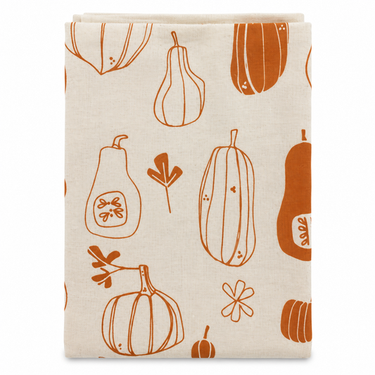 A cream colored tea towel with orange squash and pumpkin design on a white background.
