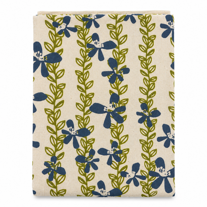 A cream colored tea towel with blue flowers and green vines design on a white background.