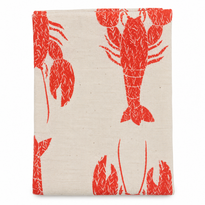 A cream colored tea towel with red lobster design on a white background.