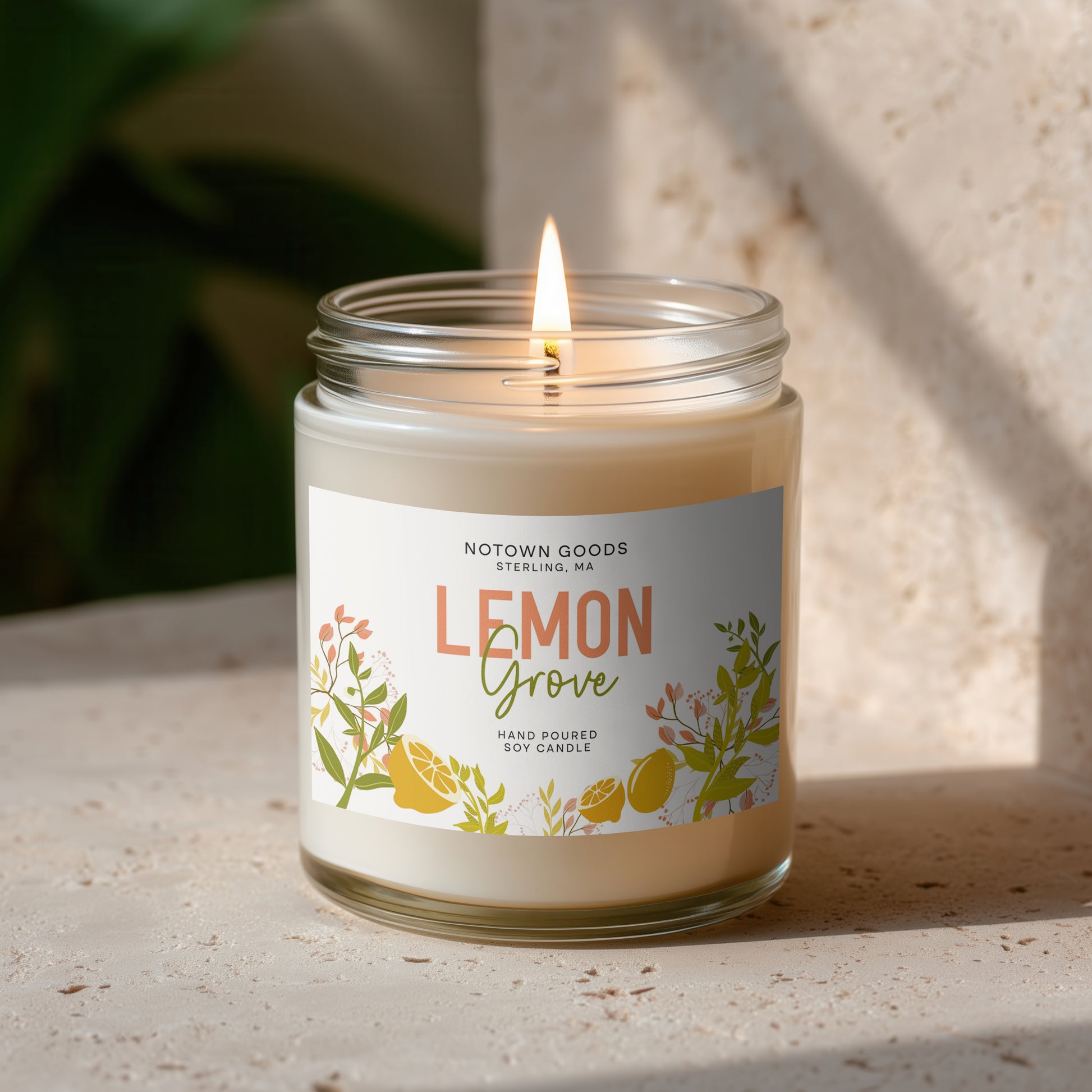 Clear jar candle with white wax and a decorative label on a blurred outdoor background.
