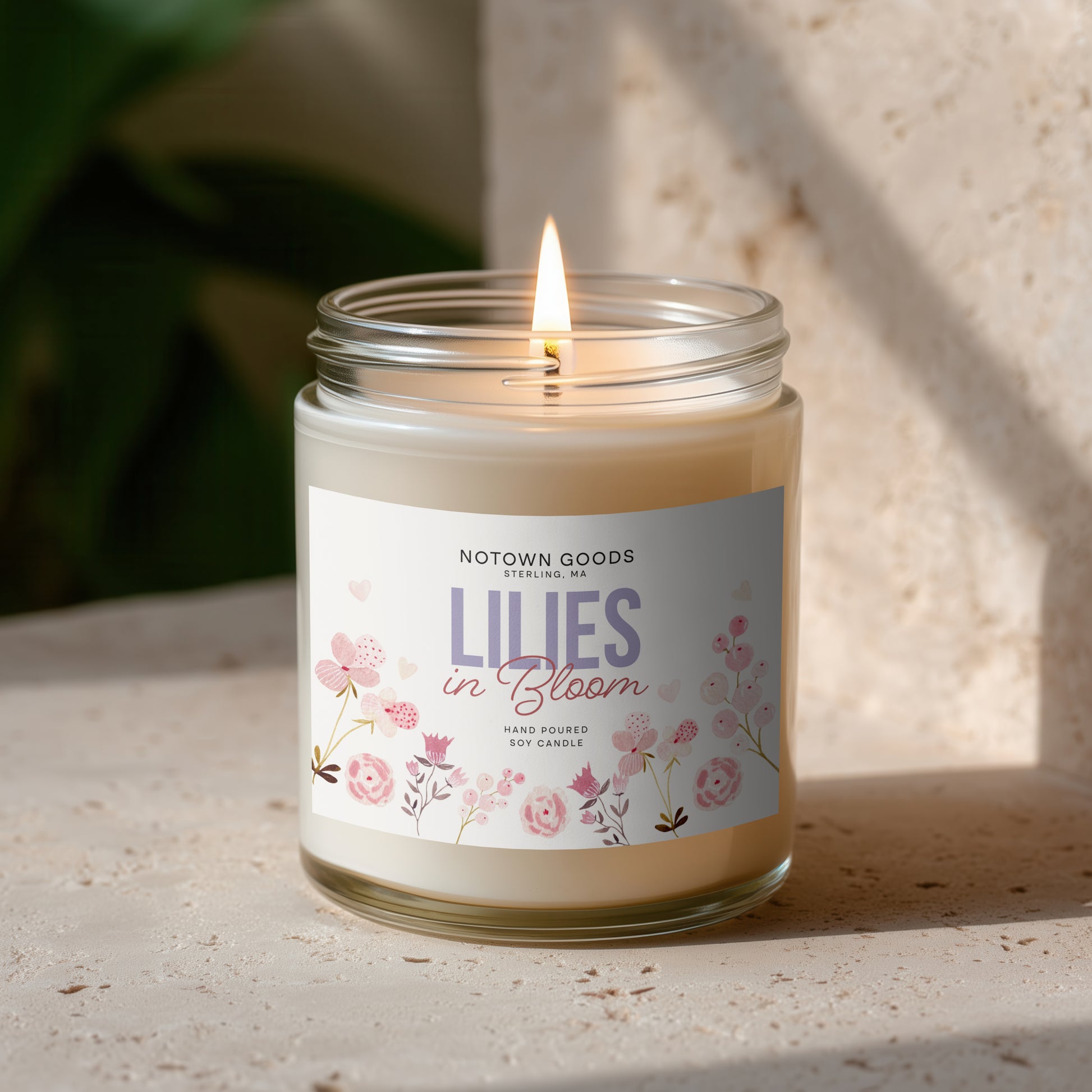 Clear jar candle with white wax and a decorative label on a blurred outdoor background.
