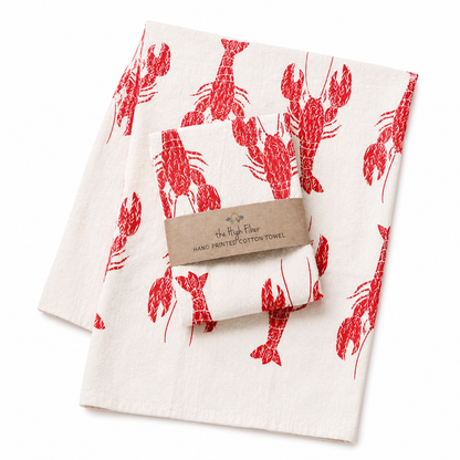 Two tea towels with red lobster print on cream colored towels on a white background.