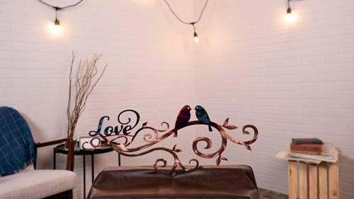 Decorative metal wall art with birds and 'Love' on a white brick wall.