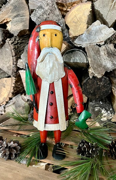 Metal Santa Claus figurine with a green umbrella on a background of wood and pine branches.