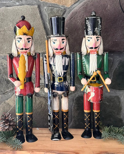 Three nutcracker figurines in red, black, and green outfits with decorative elements on a stone background.