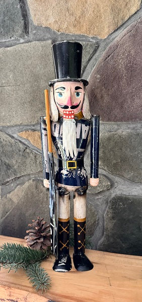 Nutcracker figurine with a top hat and rifle against a stone wall background