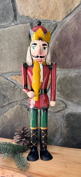 Metal nutcracker figure with a red outfit and yellow beard against a stone wall.