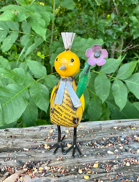 Decorative bird figurine with a flower on a wooden surface with green foliage in the background
