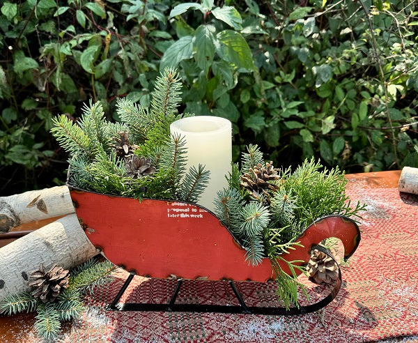 Decorative red sleigh with greenery and a candle on a patterned surface with a natural background.