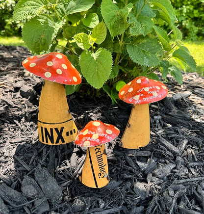 Three small metal mushroom figurines with red caps and yellow stems on mulch.