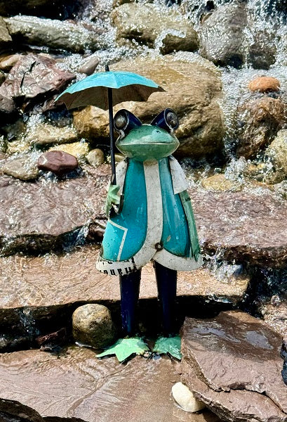 Frog figurine with a blue umbrella standing on rocks near water