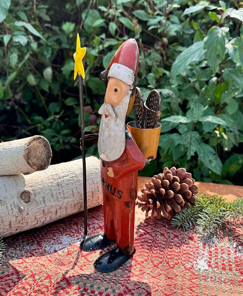 Metal Santa Claus figurine holding a star, surrounded by nature elements like logs and pinecones.