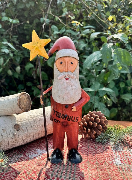 Metal Santa Claus figurine holding a star, surrounded by nature elements like logs and pinecones.