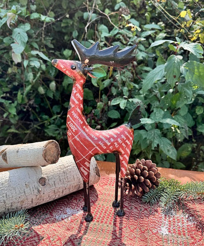 Decorative metal deer figurine on a textured surface with greenery in the background