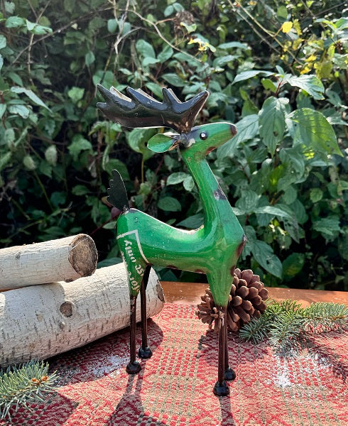 Green metal reindeer figurine with antlers on a textured surface with greenery in the background