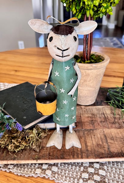 Decorative figurine of a sheep in a dress on a table with a notebook and plant.