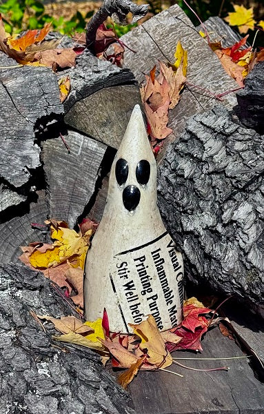Decorative ghost figure on a wooden surface with autumn leaves