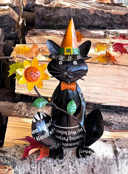 Decorative black cat figurine with a witch hat on a wooden surface with leaves.