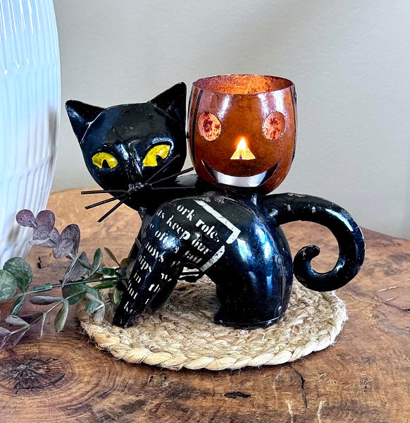 Black cat-shaped candle holder with a lit candle on a wooden surface