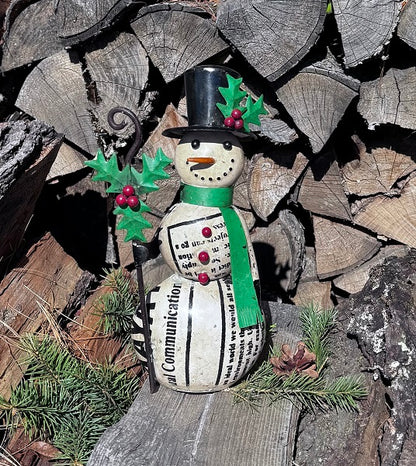 Metal snowman figurine with a top hat and green scarf on a stack of firewood.