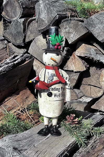 Decorative snowman figurine with top hat and holding a cardinal on a wooden log pile.