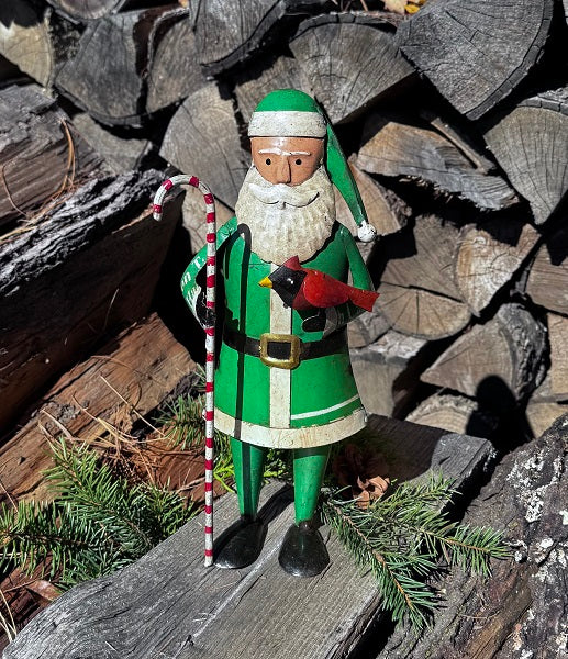 Traditional Santa Claus figurine with green suit and hat, standing on a wooden surface with logs in the background.