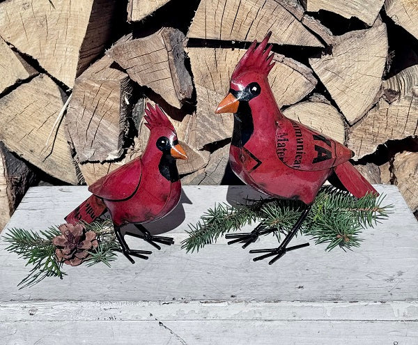 Two red cardinal bird figurines on a wooden surface with stacked logs in the background.