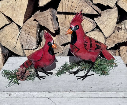 Two red cardinal bird figurines on a wooden surface with stacked logs in the background.