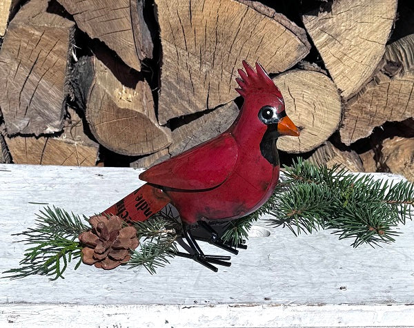 Red cardinal bird  figurine on a branch with pine cones and logs in the background