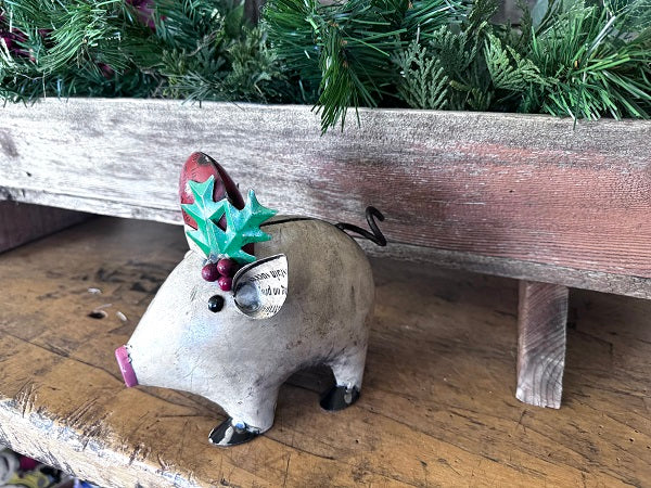 Decorative pig figurine with a red nose and green leaves on a wooden surface with Christmas decorations in the background.