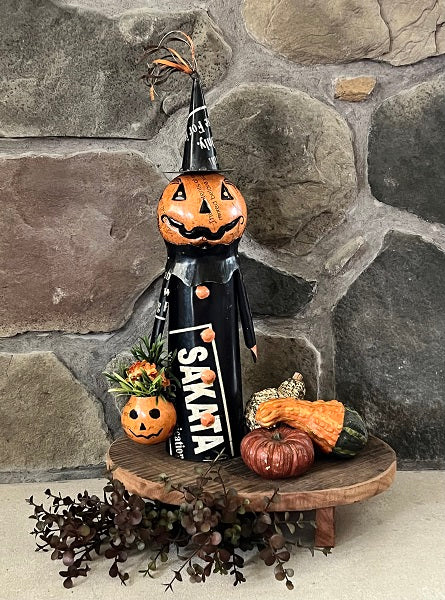 Halloween-themed decoration with a pumpkin and witch hat on a wooden stand against a stone wall.