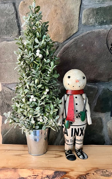Small potted tree and snowman figurine with a red scarf against a stone wall.
