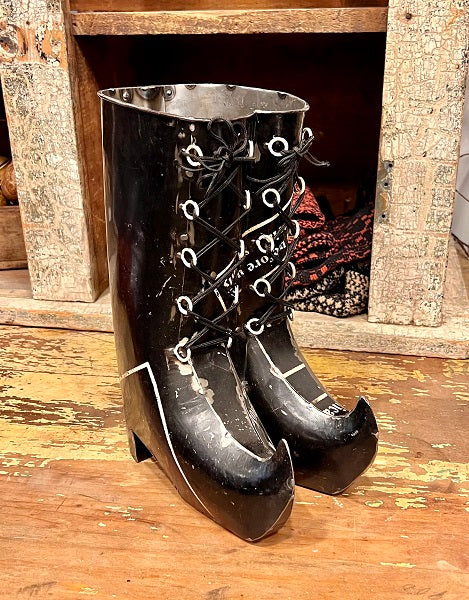 Black metal boot-shaped container on a wooden floor with a rustic background.